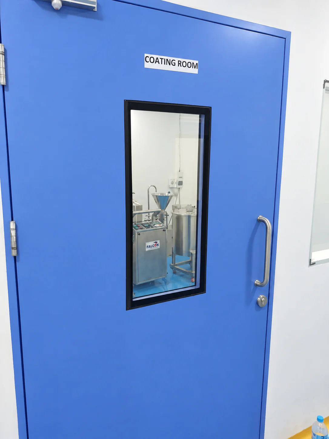 Blue coating room door with a viewing window into Healthy Health processing equipment