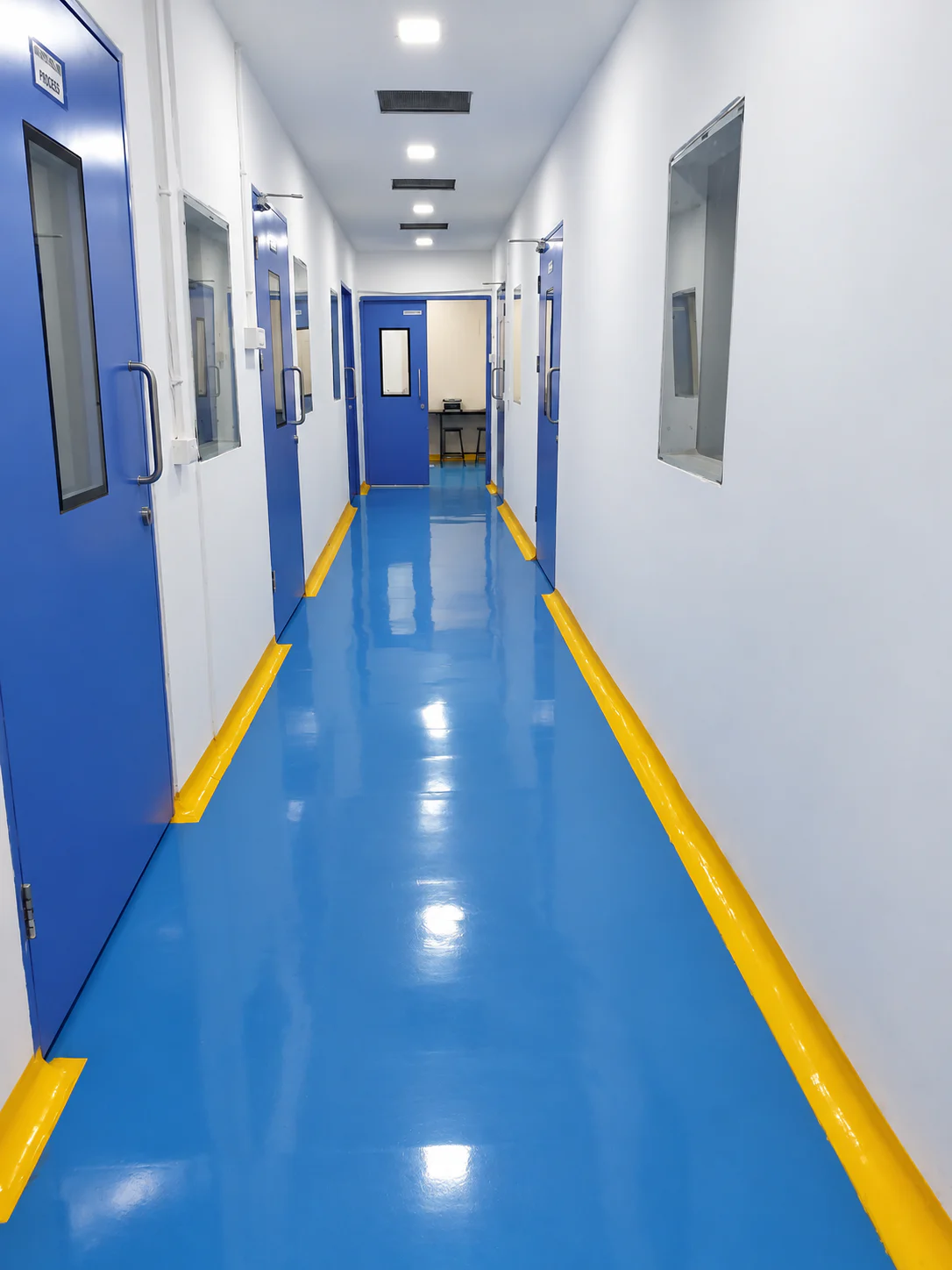 Long Healthy Health facility corridor with blue doors, blue flooring and yellow edge markings